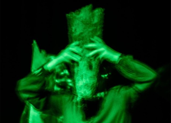 Photo d'un élève de l'option théâtre, le visage caché par un bout de bois et illuminé en vert